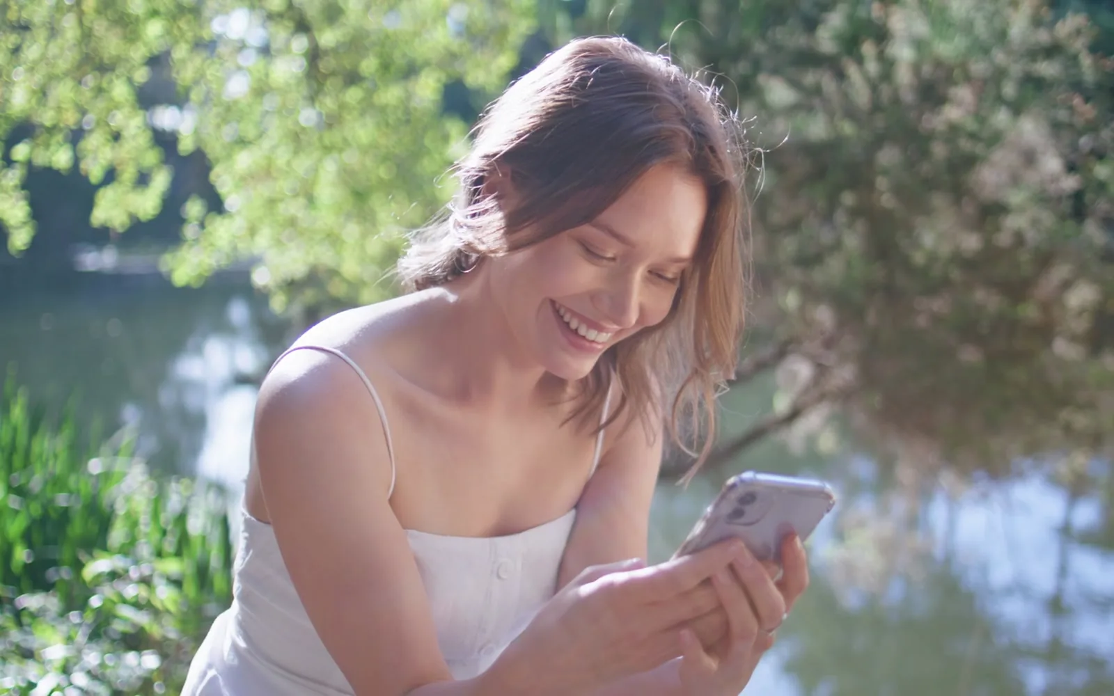 A woman smiling warmly while reading a message in golden light