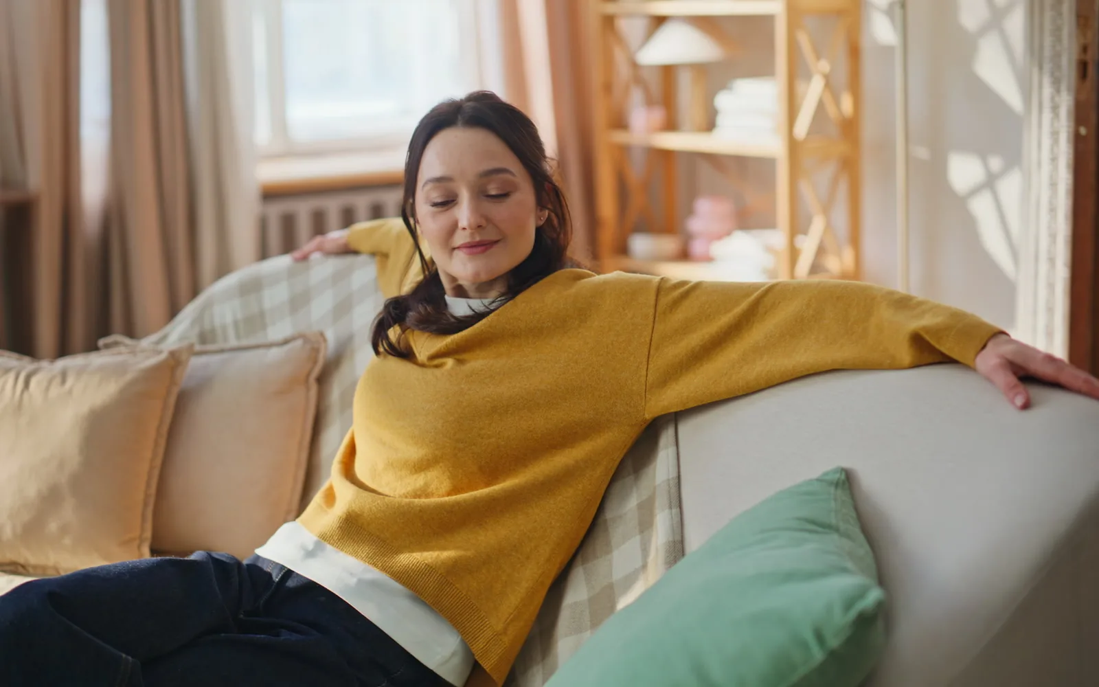 A woman settled back on a sofa in a bright, warm living room, smiling contentedly